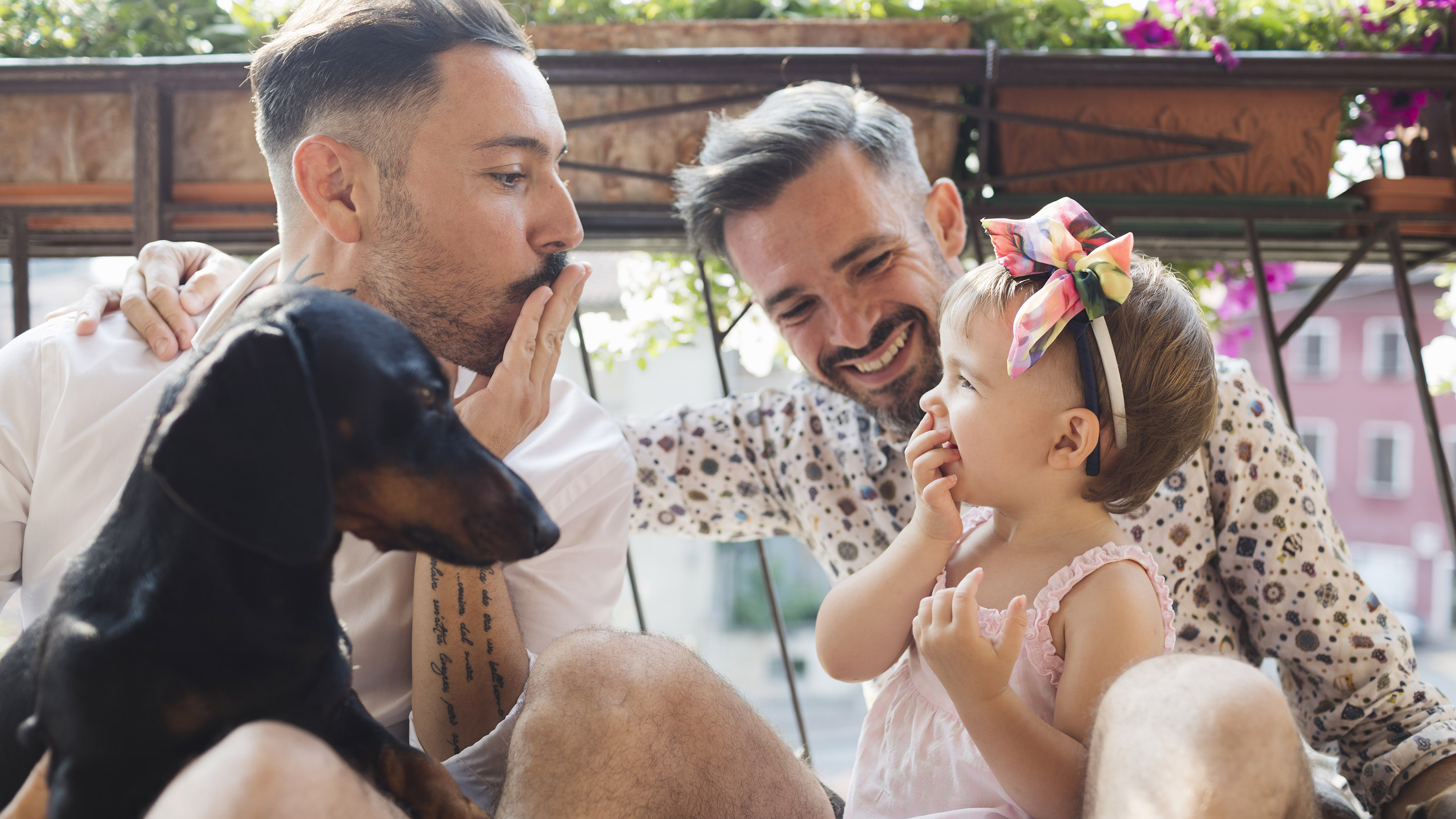 Happy gay couple with daughter and dog on balcony